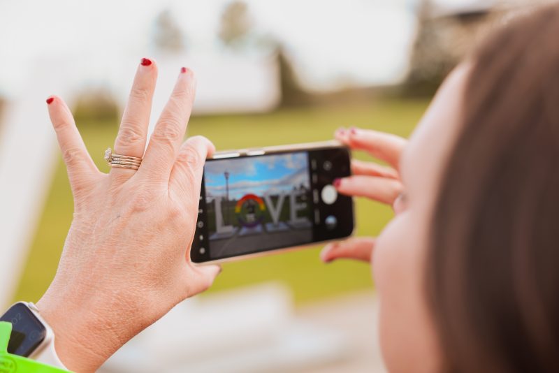 person taking a photo on a phone of event attendees and the Love sign