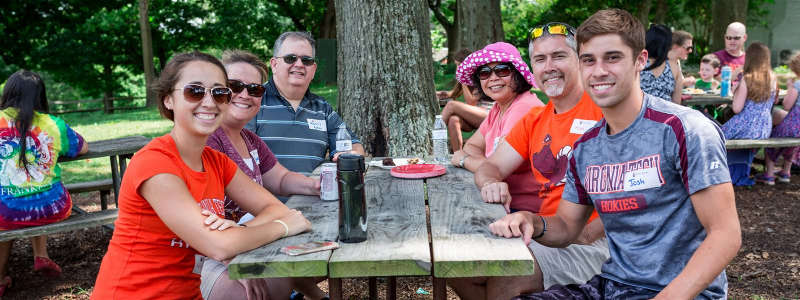 a family smiling posing outdoors at a picnic table