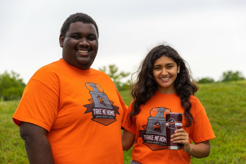 Two students pose for a photo outside wear this year's new orange Hokie Effect t-shirts