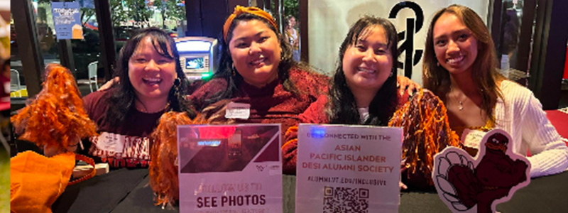 Volunteers sit at a table during an APIDAS event with signs to connect to the society